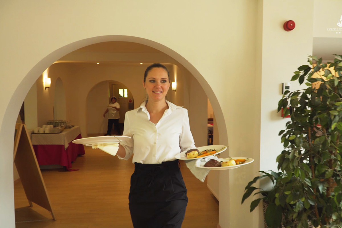 Une serveuse apporte les assiettes au restaurant de la résidence
